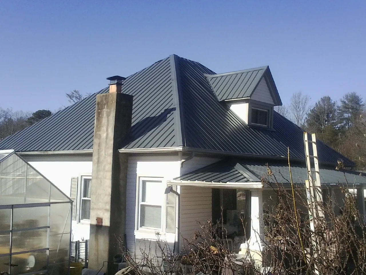 Dark blue standing seam metal roof on a white farmhouse with dormer — Slate & Tile Roof Repair by Roofing Brothers in Griswold