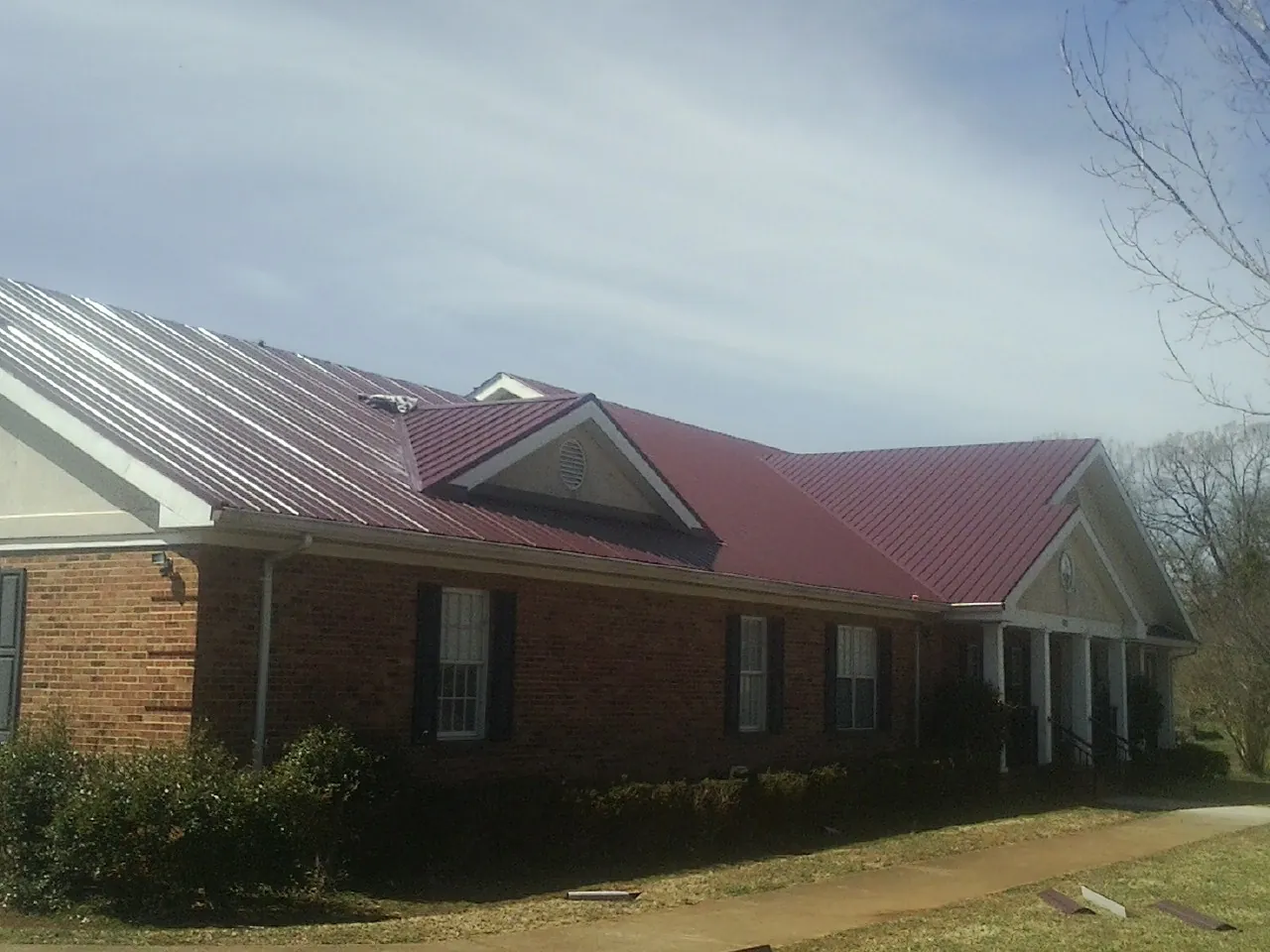 Red metal roof with gabled entries on a long brick building, from a Hail Damage Roof Repair job in Griswold