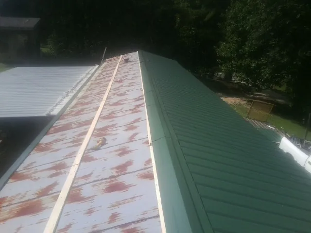 Old rusted panels beside newly installed green metal roofing — Wind Damage Roof Repair by Roofing Brothers in Griswold