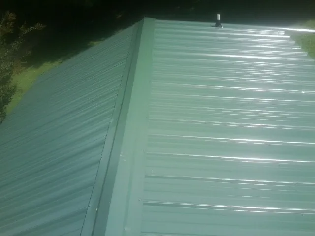 New green metal panels meeting at the ridge of a roof — Flat Roof Repair work by our crew in Griswold