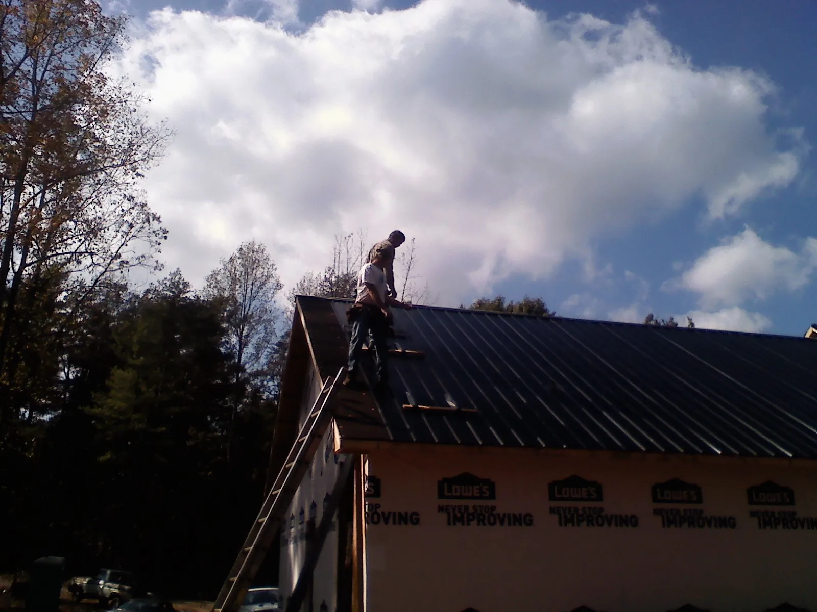 Roofer fastening dark metal panels high against a cloudy sky, from a Roof Inspection job in Griswold