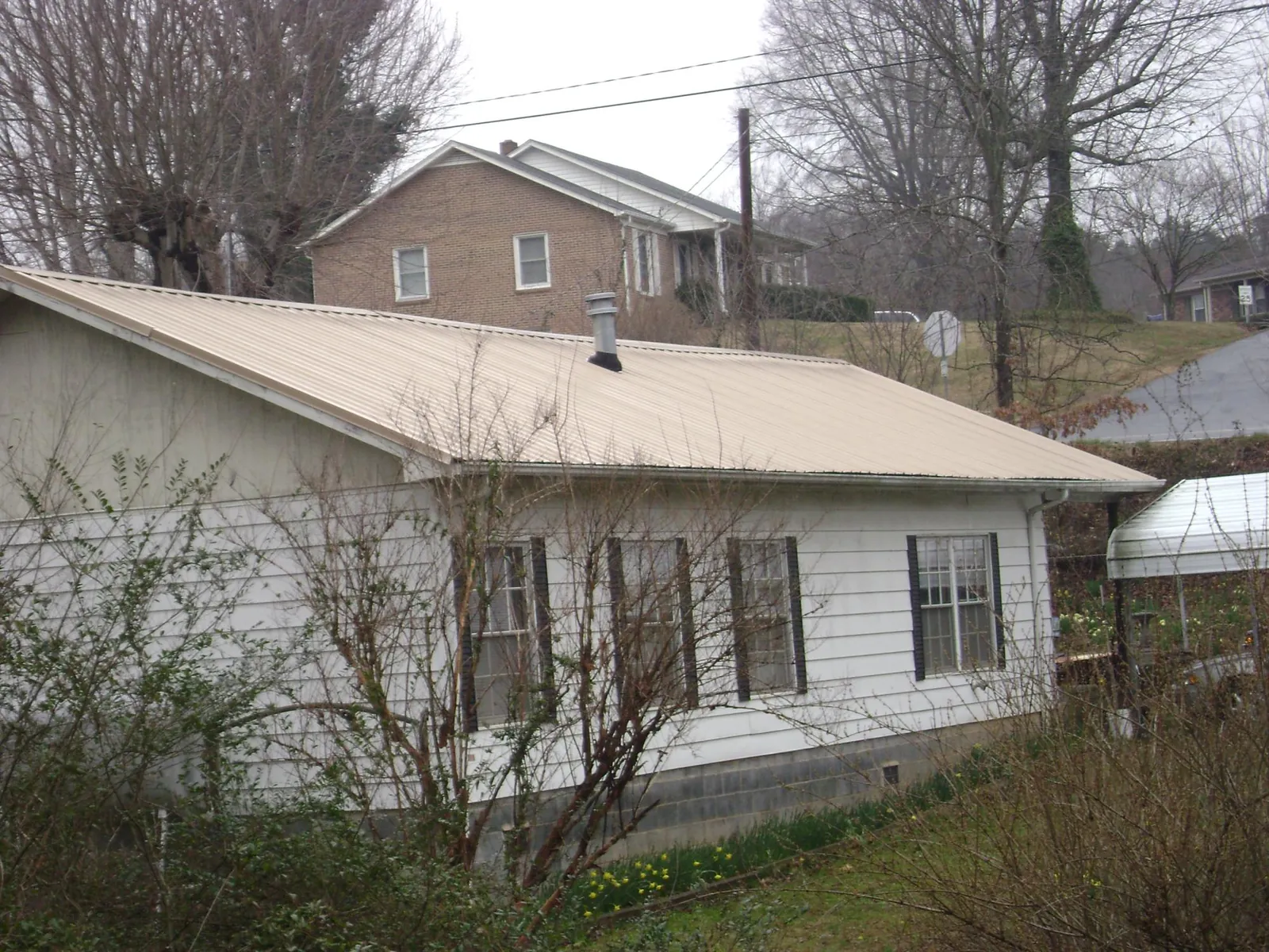 Tan metal roof on a white sided house set into a hillside — Commercial Roofing by Roofing Brothers in Griswold