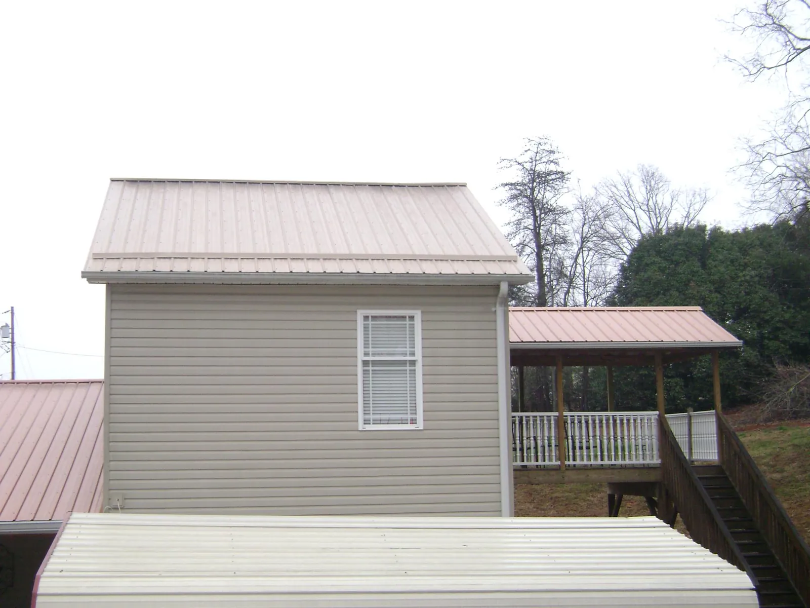 Tan metal roofs on a two story addition and attached porch, from a Roof Replacement job in Griswold