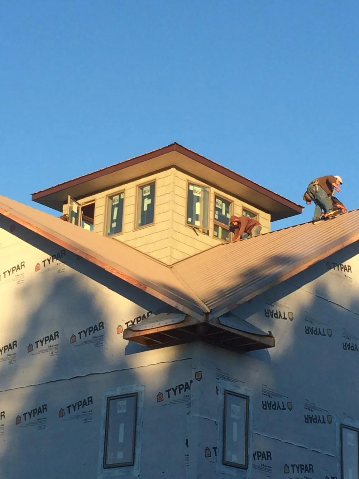 Roofers working around a rooftop cupola on a new metal roof at sunset — Roof Waterproofing in Griswold by Roofing Brothers